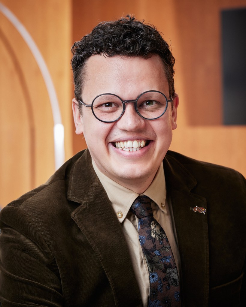 Headshot of Professor Kieran Fenby-Hulse wearing a moss green corduroy jacket and smiling into camera.